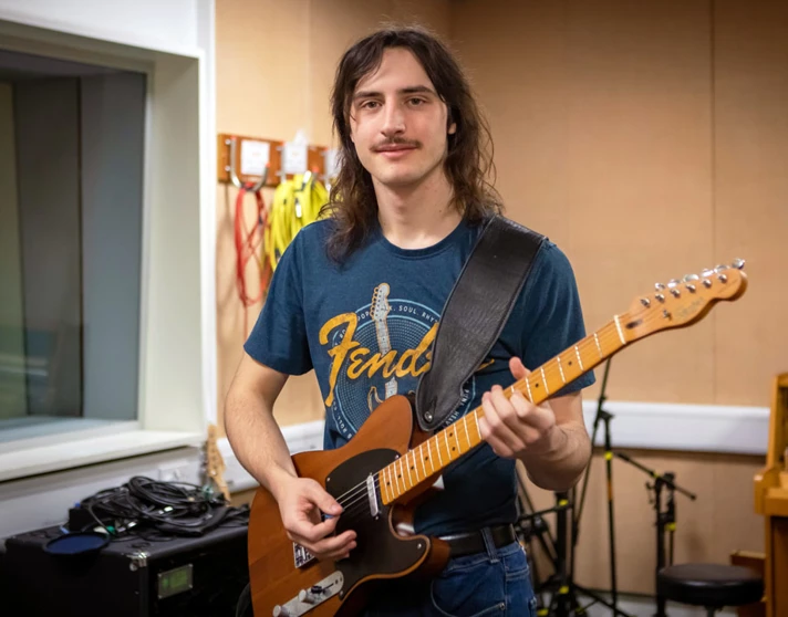 A guitarist smiling while playing a Fender Telecaster in a practice room. A guitarist smiling while playing a Fender Telecaster in a practice room.